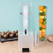 A clear plastic beverage dispenser with ice and fruit in containers including oranges.