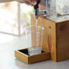 A hand pouring water into a clear glass on a Cal-Mil Madera rustic pine drip tray.