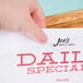 A hand holding a paper with the words "daily special" on a wood display stand with the Cal-Mil Madera Displayette.