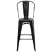 A Flash Furniture black metal bar stool with a backrest and drain hole seat.