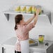 A woman in a white apron putting a can of food on a Regency stainless steel wall shelf.