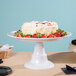 An Elite Global Solutions white melamine plate stand on a table with a cake and strawberries.