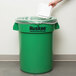 A person placing a white lid on a Continental green trash can.