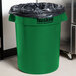 A close-up of a green Continental 32 gallon round trash can with black plastic on top.