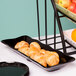 The Bakers black scalloped melamine tray with croissants and fruit on a table.