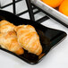 The Bakers black scalloped melamine tray holding croissants and oranges.