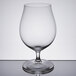 A Spiegelau stemmed pilsner glass filled with beer on a reflective surface.