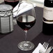 A close-up of a Spiegelau Authentis Bordeaux wine glass filled with red wine on a table.