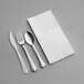 A white linen-feel napkin and silver plastic cutlery on a gray surface.