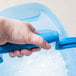 A hand holding a blue San Jamar ice scoop in a San Jamar blue ice tote.