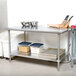 An Advance Tabco stainless steel work table with a metal shelf holding food containers.