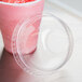 A Dart clear PET plastic dome lid on a plastic cup of pink smoothie with a straw.