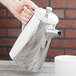 A hand holding a Vollrath Triennium stainless steel coffee pot over a white mug.