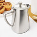 A Vollrath stainless steel creamer on a table with pastries.