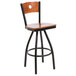 A BFM Seating black metal bar stool with a cherry wood back and swivel seat.