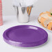 A stack of Creative Converting amethyst purple paper plates next to a silver bucket of sandwiches.