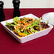 A white American Metalcraft square shallow melamine bowl filled with salad on a table with a black pepper shaker.
