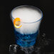 A clear plastic rocks glass with a blue liquid and an orange peel.