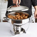 A person holding a Vollrath Orion small round chafing dish lid over a bowl of food.