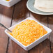 An American Metalcraft white melamine serving bowl filled with shredded cheese on a table.