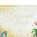 A blue metal counter with a Hoffmaster Welcome Paper Placemat with a sign that says "Welcome to our place" and flowers.