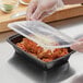 A person in gloves holding a Choice black rectangular microwavable container with spaghetti and a plastic lid over it.