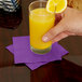 A hand holding a glass of orange juice on a purple Creative Converting beverage napkin.