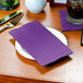 A table set with a plate and Creative Converting Amethyst Purple dinner napkin.