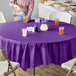 A purple Creative Converting plastic table cover on a table with a glass of orange juice.