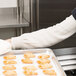 A person wearing Cordova heat resistant sleeves holding a tray of pastries.