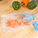 A person in blue gloves using an ARY VacMaster full mesh vacuum packaging bag to hold carrots.