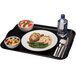 A black Cambro cafeteria tray with food, a bowl of fruit salad, and silverware on a napkin.