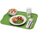 A lime green Cambro rectangular tray with food, a plate of food, and a bowl of vegetables on it with a fork and knife.