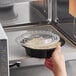 A hand placing a Choice black plastic container of food into a microwave.