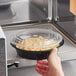 A hand holding a Choice black plastic microwavable container of food in a microwave.