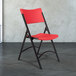 A black metal National Public Seating folding chair with red plastic back and seat.