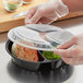 A person in gloves putting food into a Choice 3-compartment plastic container with a lid.
