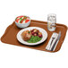 A rectangular brown Cambro tray with food, a fork, and a glass of water on a table.