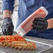 A person in gloves using a Tablecraft INVERTAtop squeeze bottle to pour sauce onto ribs on a rack.
