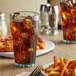 A jade plastic tumbler of ice tea with ice cubes on a table with a plate of fries.