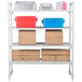 A white Cambro Camshelving® premium shelving unit with 4 vented shelves holding brown, blue, and red containers and brown boxes.