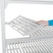 A person's hand holding a white Cambro Camshelving Premium vented shelf.