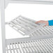 A person's hand attaching a white vented shelf to Cambro Camshelving.