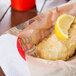 American Metalcraft newspaper deli wrap with a fried fish fillet and a lemon wedge.