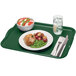 A Cambro Sherwood Green rectangular tray with food, a fork, and a knife on a napkin.