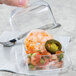 A person holding a clear plastic container with shrimp, jalapenos, and salsa.