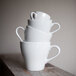 A stack of Tuxton porcelain white cappuccino mugs.
