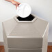 A hand putting a white plate into a Commercial Zone hexagonal beige outdoor trash can.