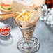 A basket of french fries and a burger wrapped in newspaper on a table.