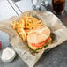 A burger and fries on American Metalcraft newspaper deli wrap in a basket.